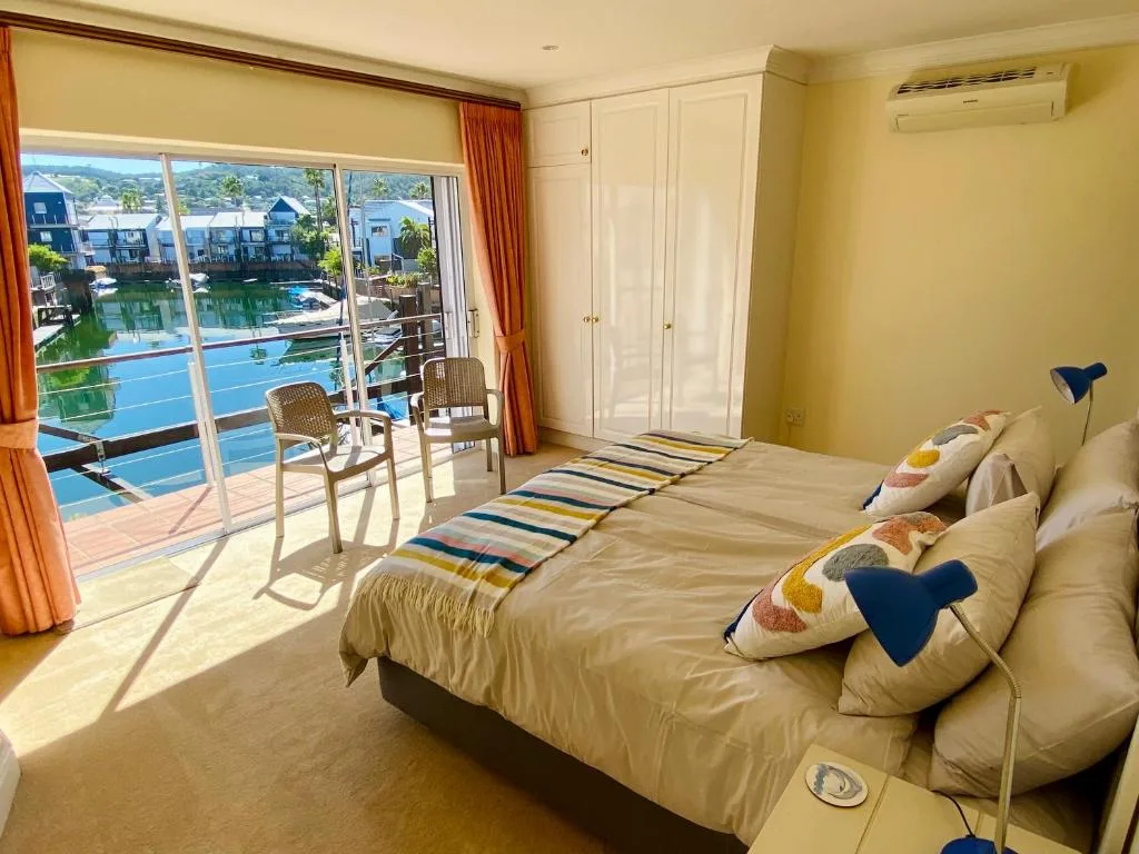 Bright bedroom with bed overlooking lagoon and waterfront buildings through glass doors