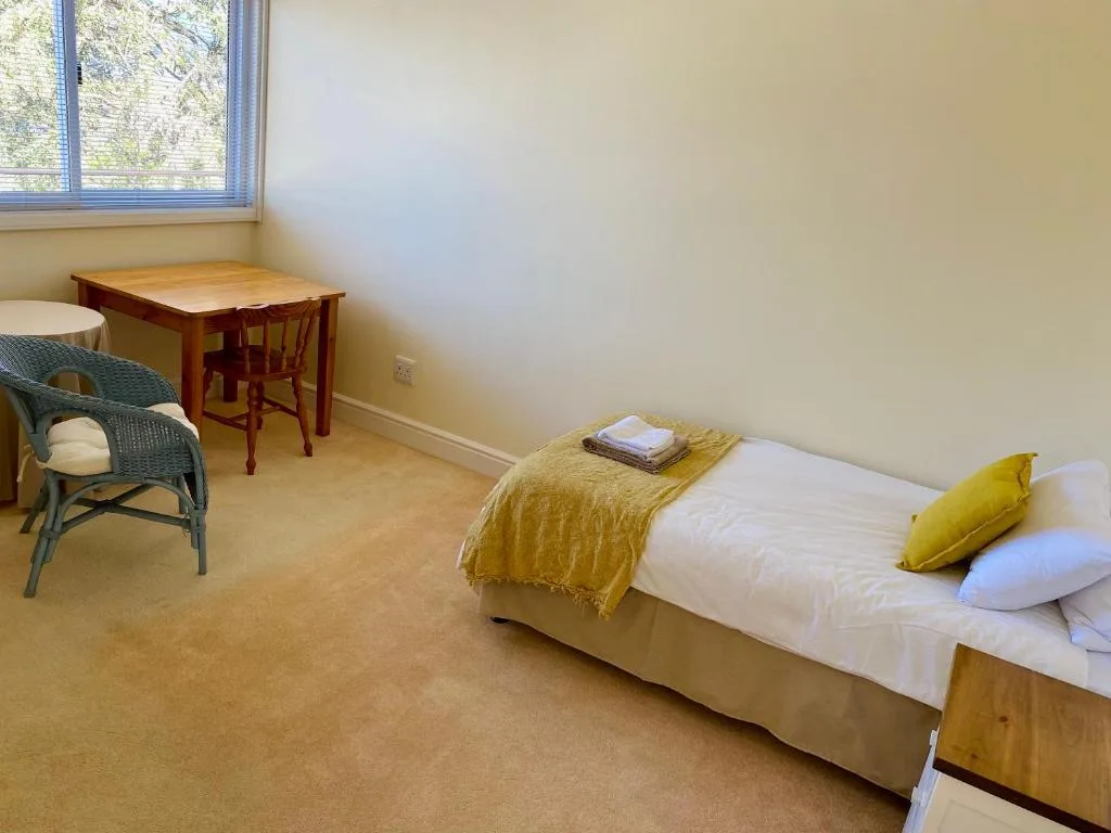 Bright bedroom with queen bed, yellow cushion, wooden desk, and natural light