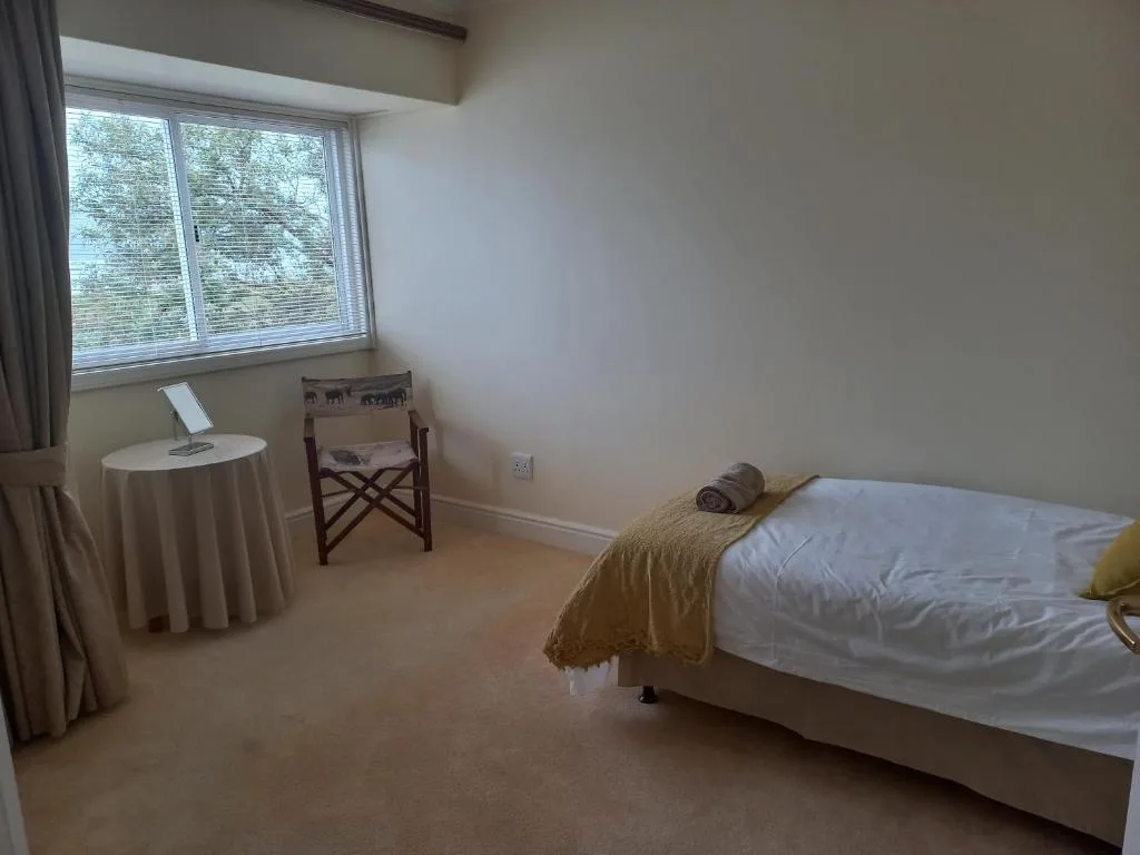 Bright bedroom with white bed, wooden chair, and garden view windows