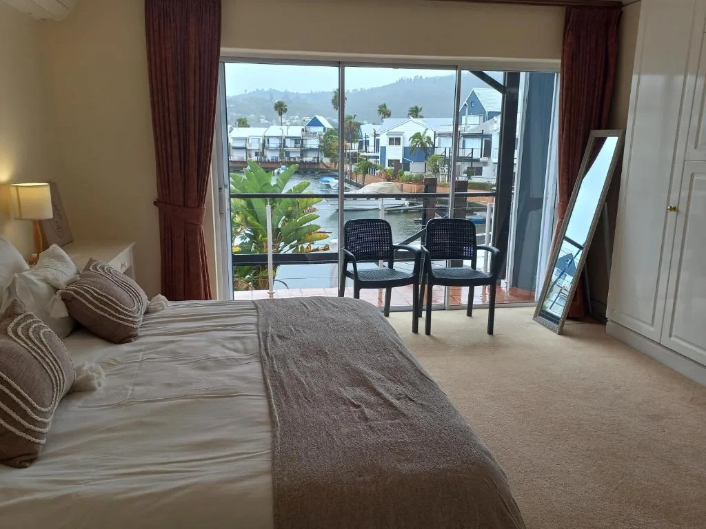 Bedroom with bed overlooking waterfront homes and mountains through large windows