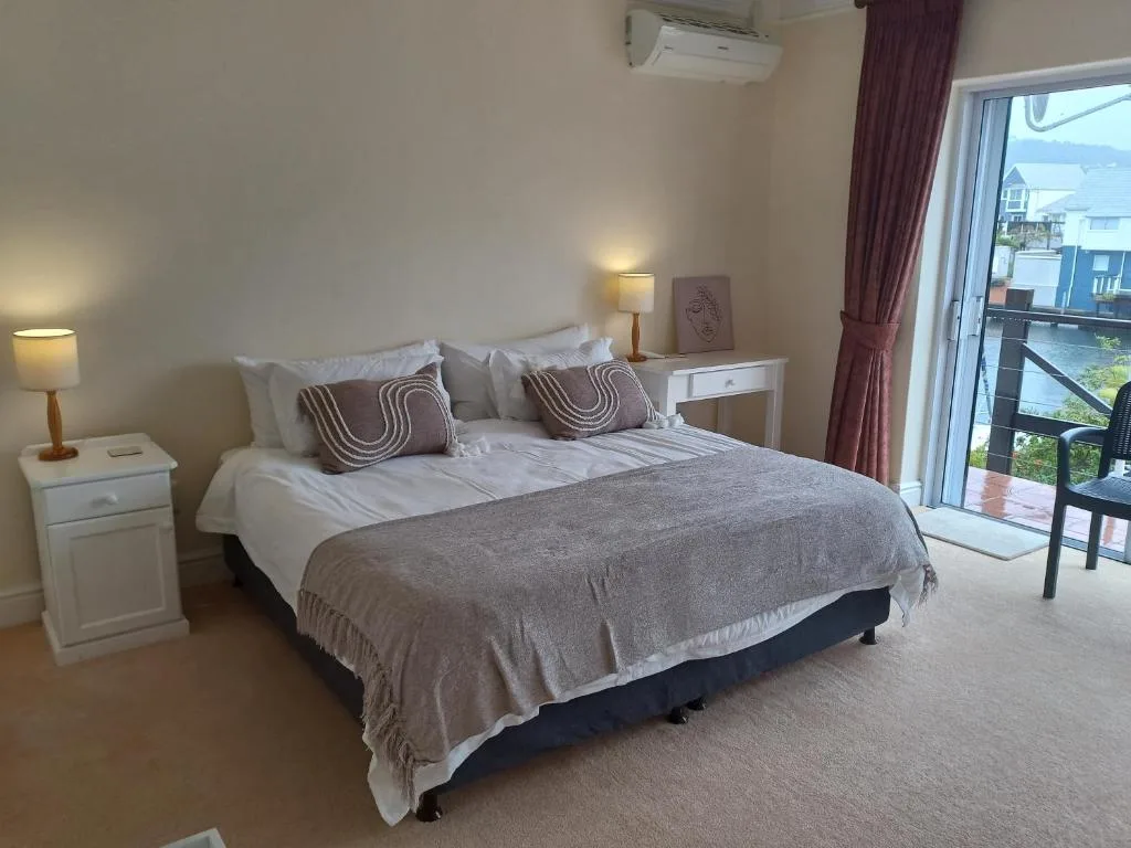 Spacious bedroom with queen bed, neutral décor, and waterfront balcony access