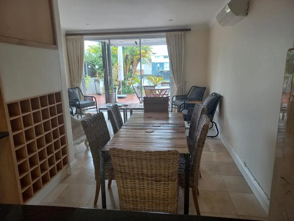 Dining area with wicker chairs overlooking garden and waterfront views through glass doors