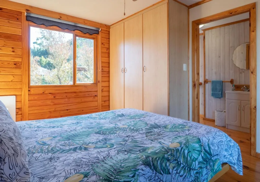 Wooden bedroom with double bed, wardrobe, and ensuite bathroom visible through open door