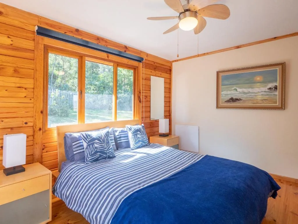 Bright bedroom with wooden walls, queen bed, and large windows overlooking garden