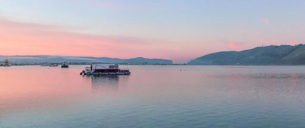 Serene lagoon at sunrise with moored boats and forested mountains