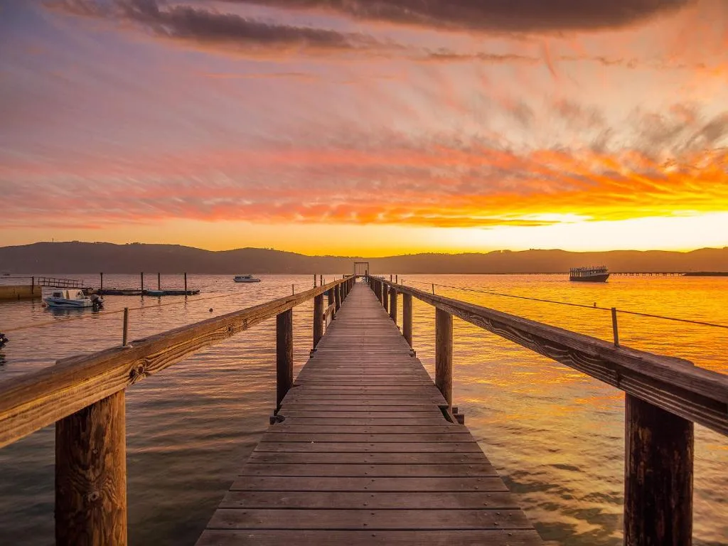 Wooden jetty extending into lagoon at golden sunset with mountains