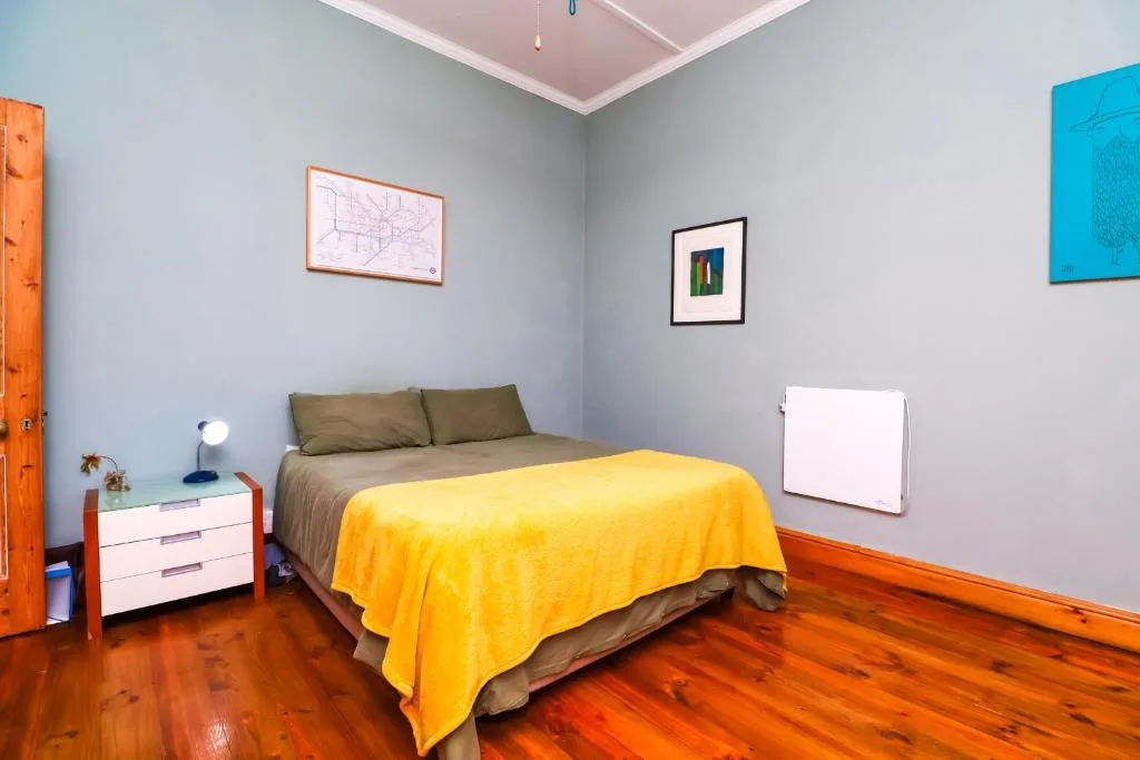Bright bedroom with yellow bedspread, olive green pillows, wooden floors