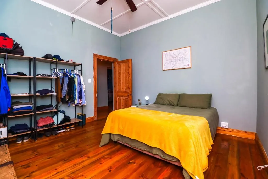 Spacious bedroom with wooden floors, yellow bedcover, and storage shelving