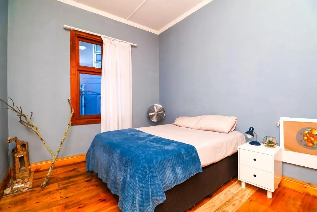 Bright bedroom with blue bedcover, wooden floors, and red-framed window