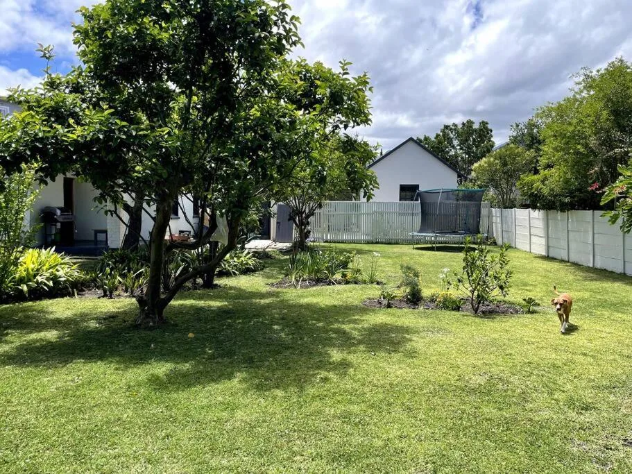 White cottage with manicured garden, mature trees, and fenced yard