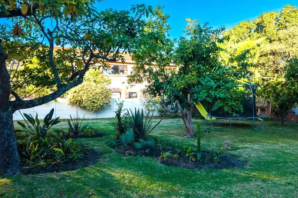 White building with lush green gardens, mature trees, and trampoline visible