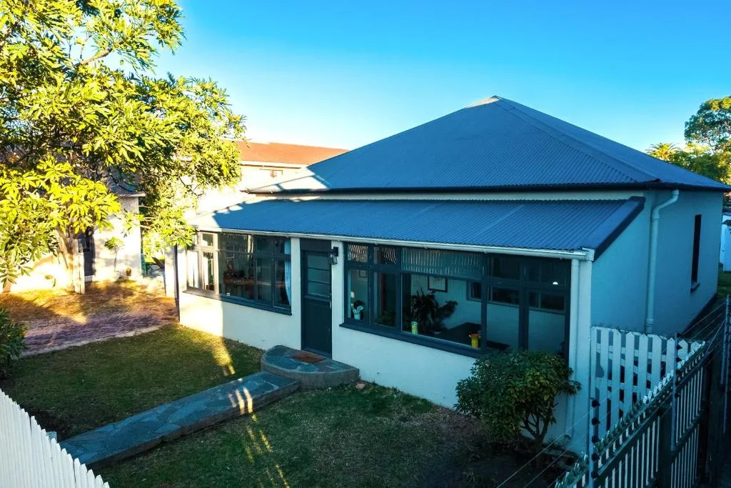 Modern home with blue corrugated roof and white railings, sunny garden setting