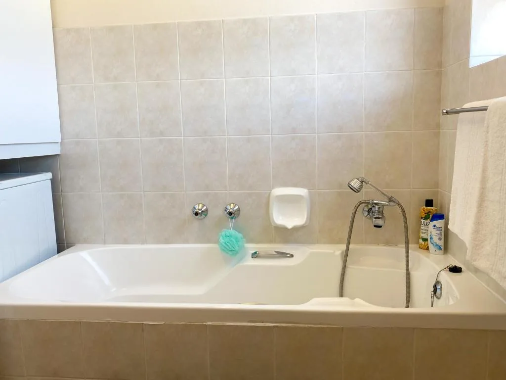 Clean bathtub with tiled walls, shower fixture, and bathroom amenities