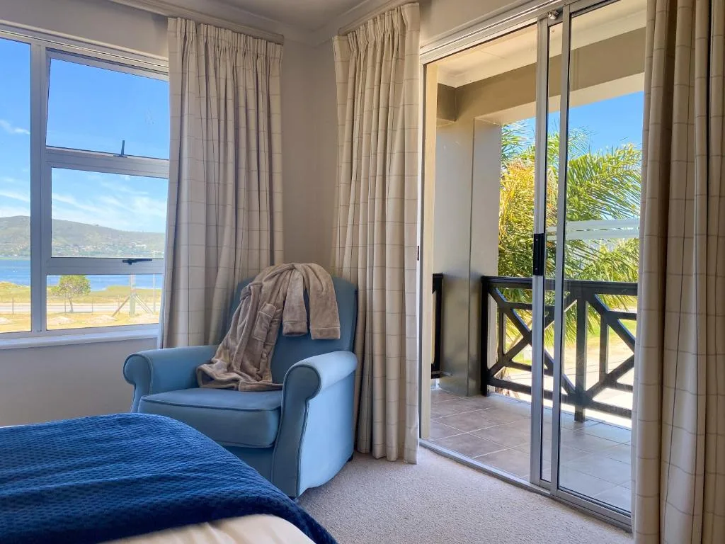 Bedroom with blue armchair, water view through windows and glass doors