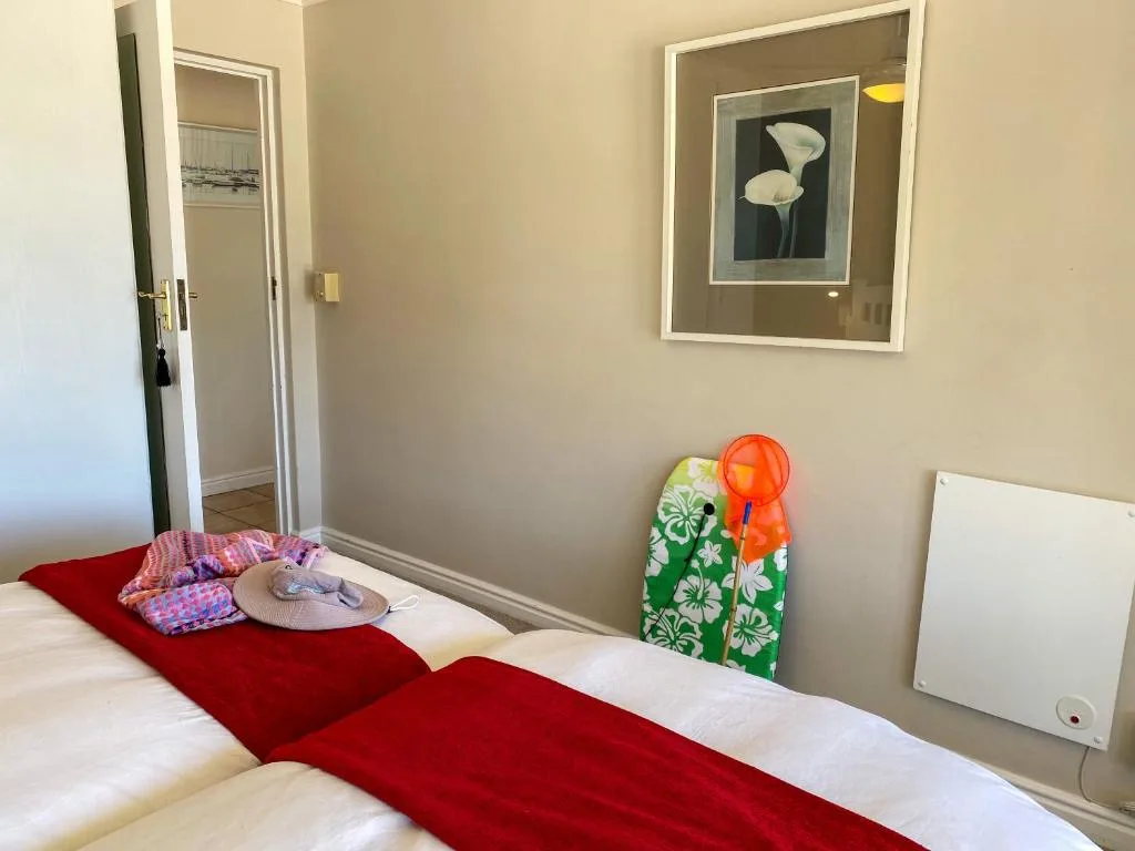 Bright bedroom with white bedding, red throw, and framed floral artwork on walls