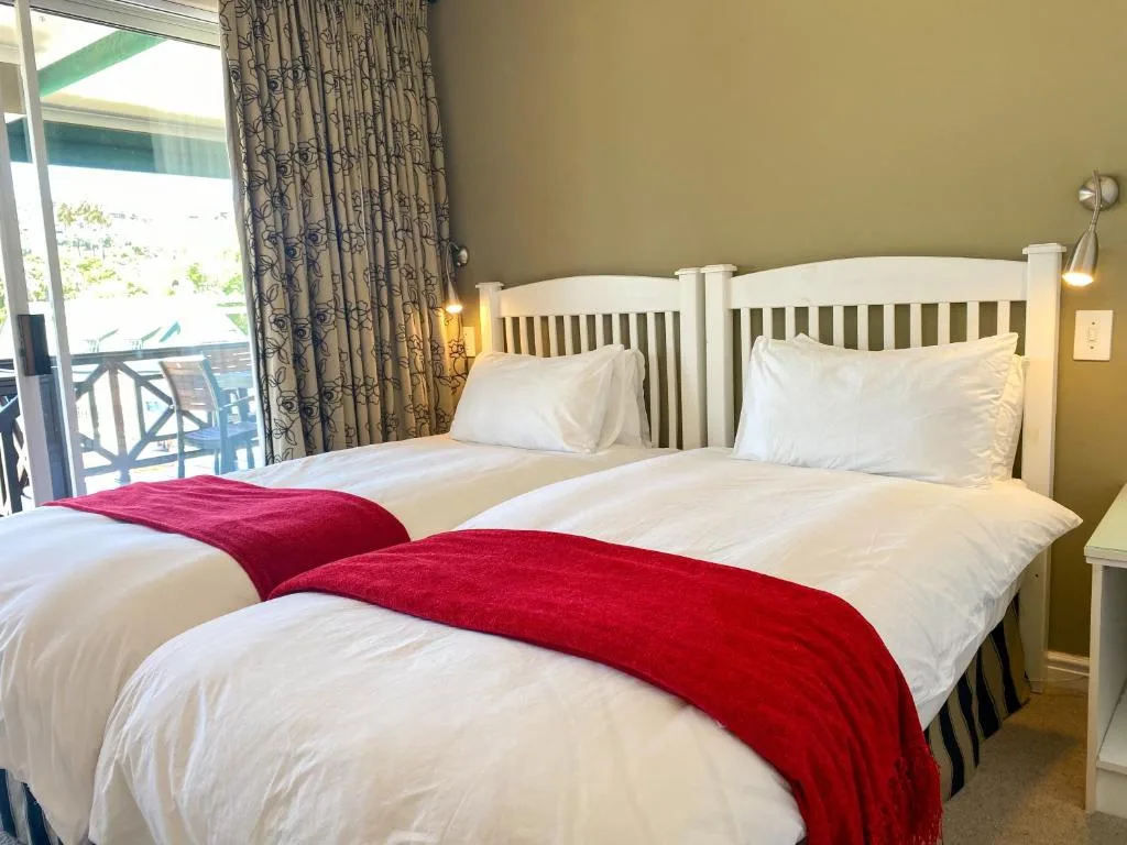Twin beds with white linens and red throws in bright bedroom with deck view