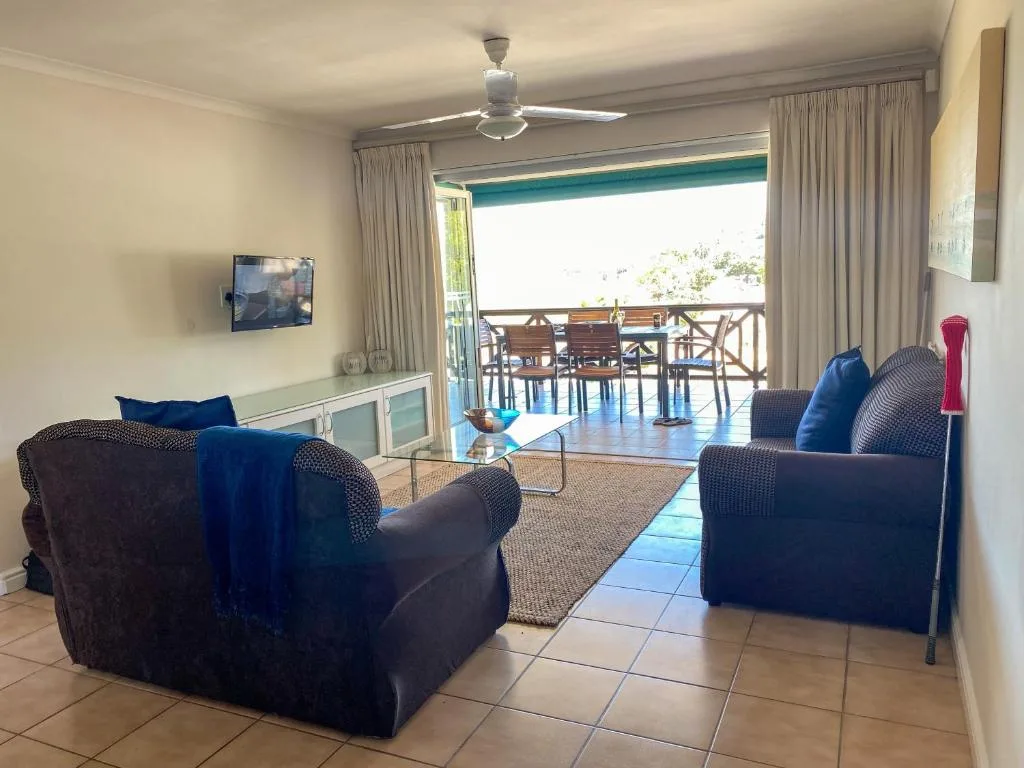 Spacious lounge with dark upholstered armchairs, TV, and open deck access