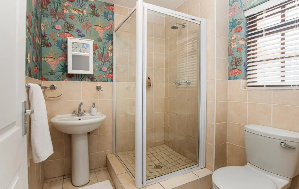Bathroom with pedestal sink, shower stall, and colorful fish wallpaper accent