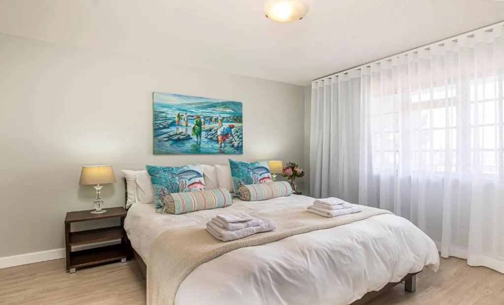 Bright bedroom with double bed, coastal artwork, and sheer curtains