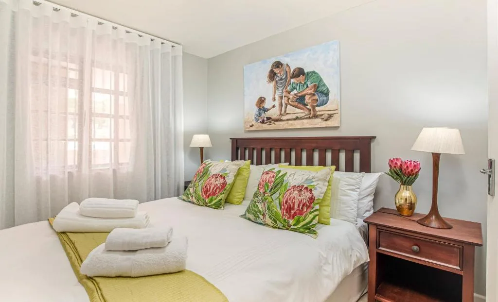 Bright bedroom with queen bed, floral pillows, wooden headboard, and fresh flowers