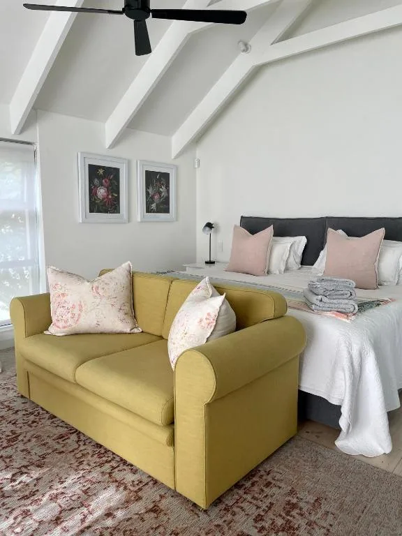 Bright bedroom with queen bed, yellow armchair, and vaulted ceilings with fan