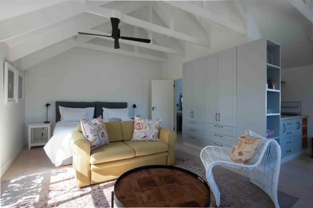 Bright open-plan lounge with yellow sofa, wicker chair, and bed in background