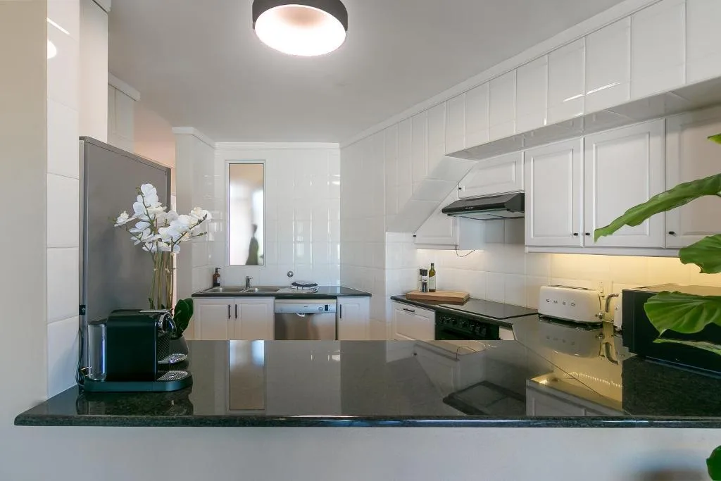 Modern white kitchen with granite countertop, stainless steel appliances, and fresh flowers