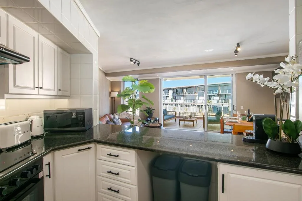 Modern kitchen with white cabinetry, dark countertops, and waterfront views through glass doors