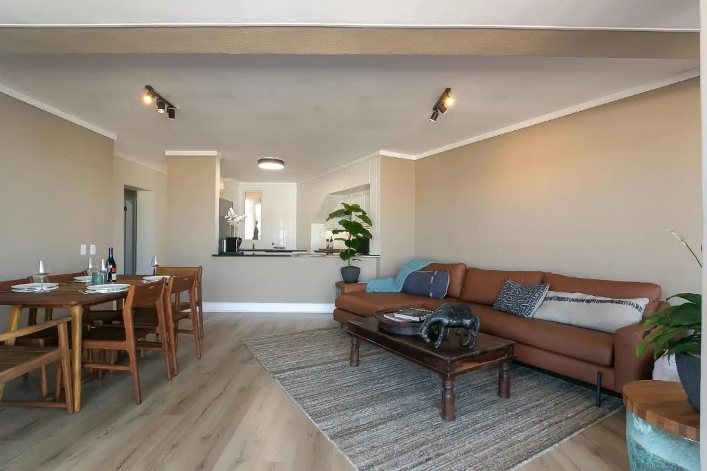 Open-plan lounge with brown leather sofa, wooden dining table, and modern kitchen