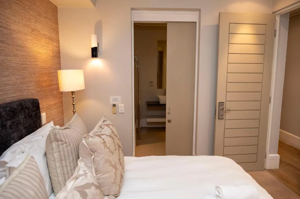 Modern bedroom with bed, textured accent wall, bedside lamp, and ensuite bathroom access