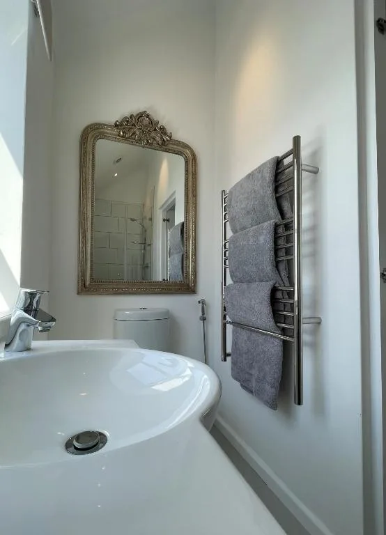 Modern bathroom with ornate mirror, white sink, and heated towel rack