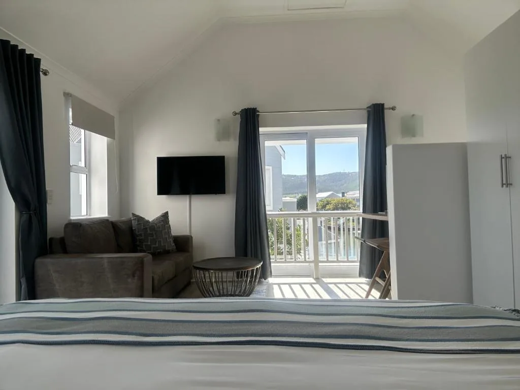 Bright bedroom with bed, lounge area, TV, and mountain views through glass doors