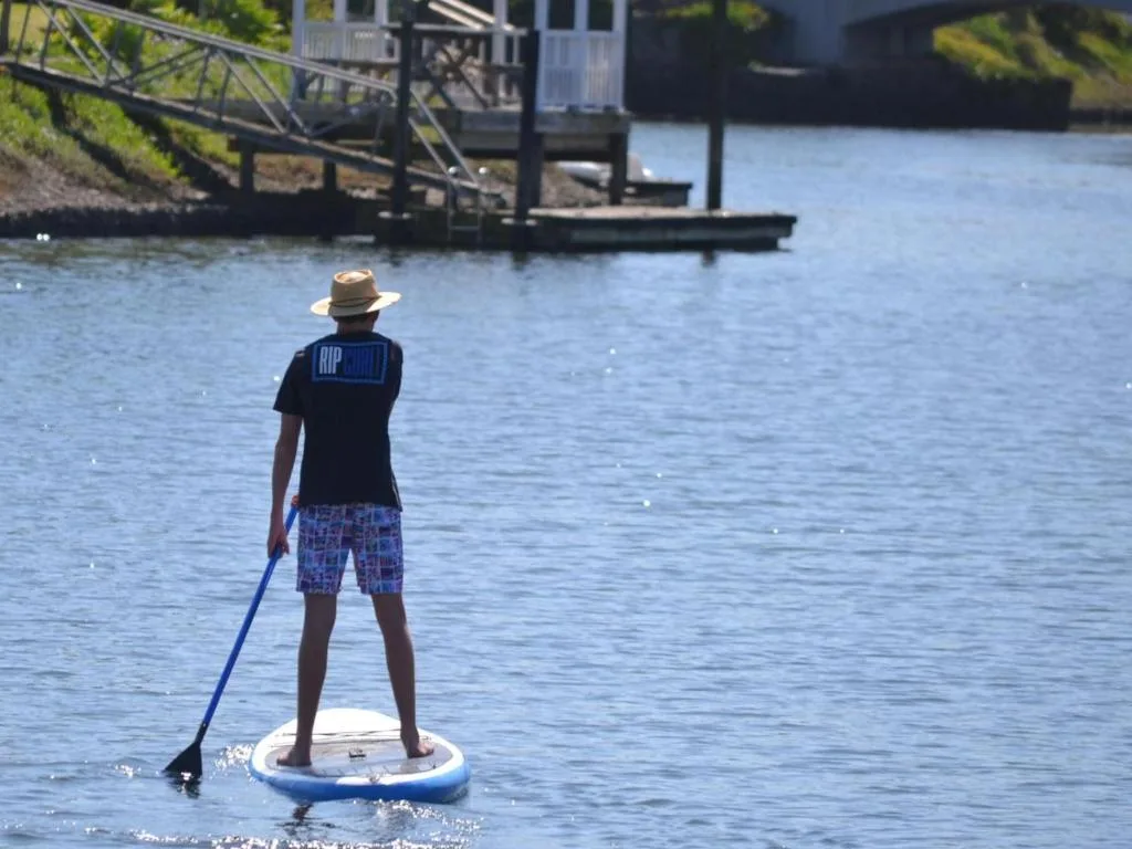 Waterfront view with person paddleboarding on lagoon, jetty and property visible
