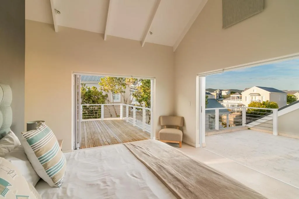 Bright bedroom with bed, striped pillows, and open doors to deck