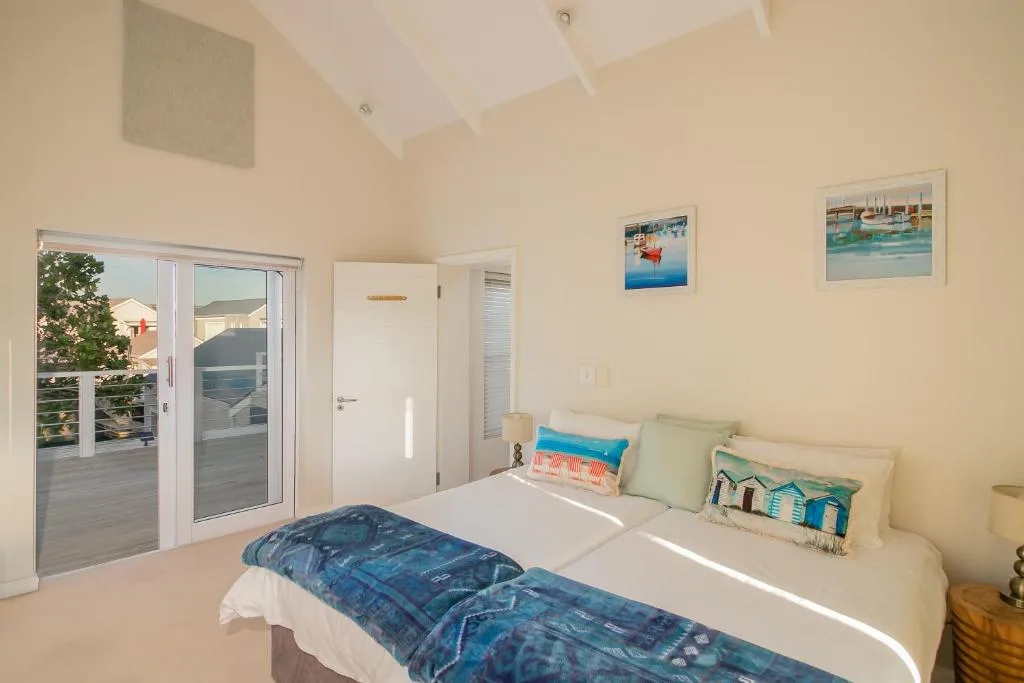 Bright bedroom with double bed, coastal artwork, and deck access doors
