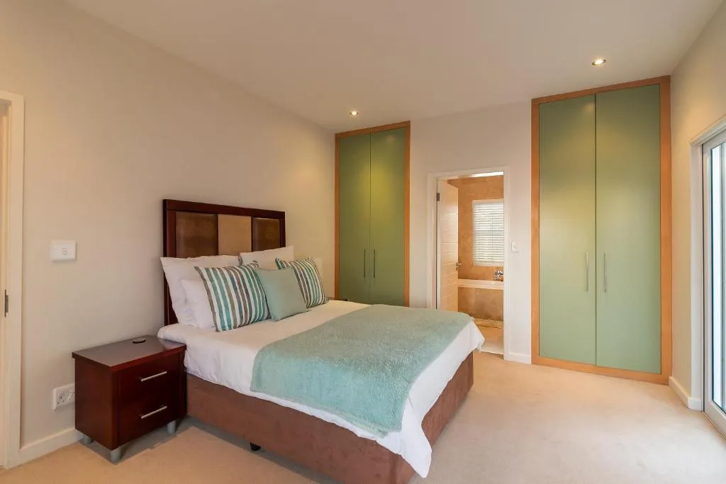 Spacious bedroom with wooden bed frame, striped pillows, and green built-in wardrobes