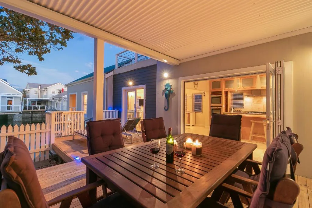 Evening deck with dining table, chairs, and illuminated kitchen view beyond