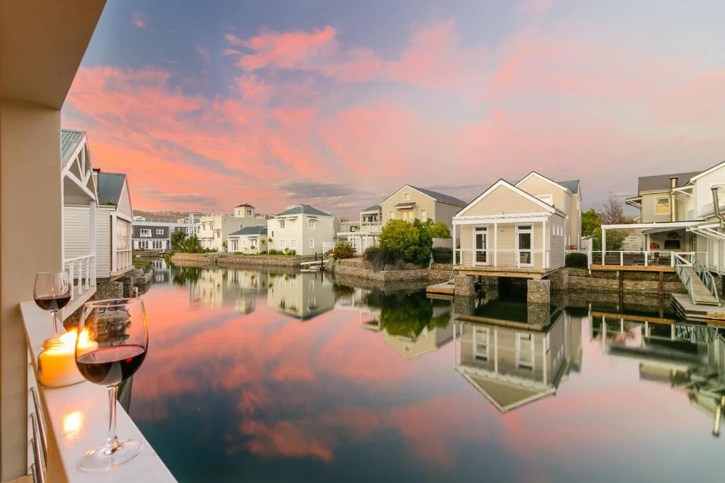 Sunset over calm lagoon with waterfront homes and wine glasses on deck