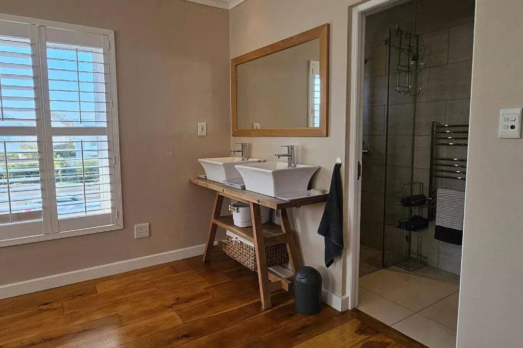 Modern bathroom with dual vanity sink, wooden mirror frame, and rainfall shower