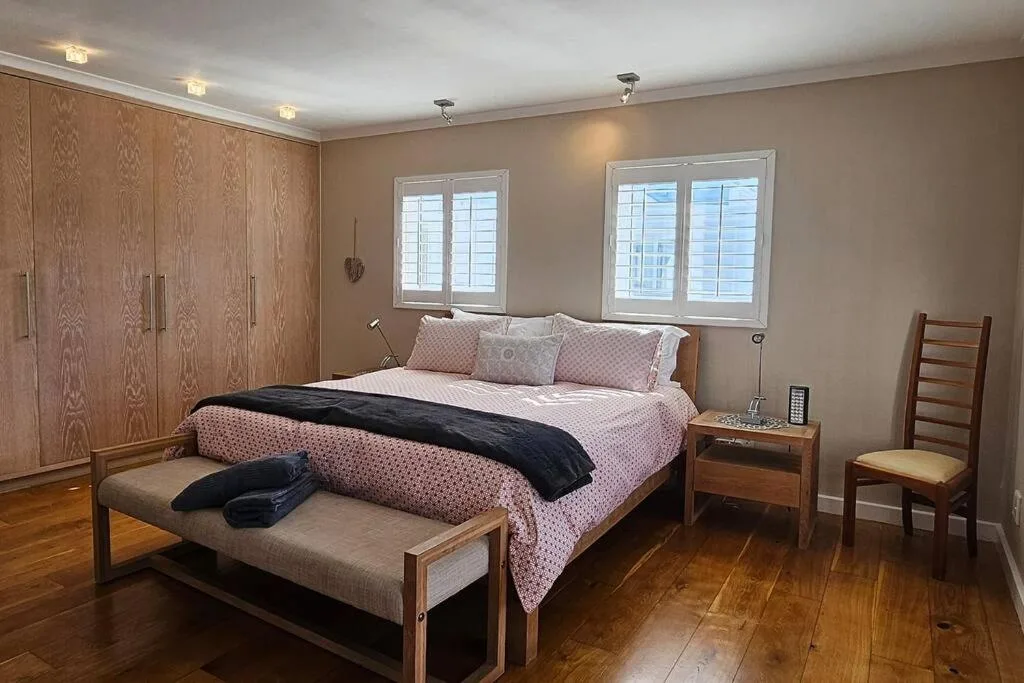 Spacious master bedroom with wooden bed, pink bedding, and large windows
