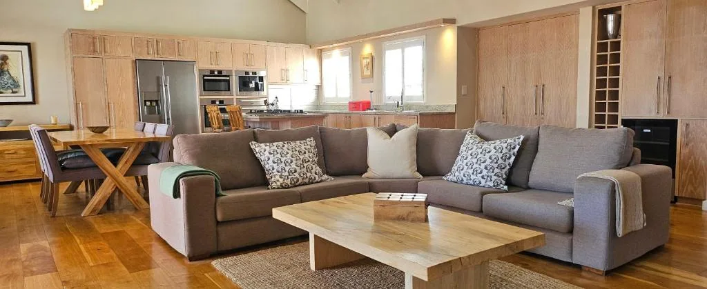 Open-plan lounge with grey sectional sofa, wooden coffee table, and kitchen beyond
