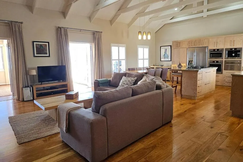 Spacious open-plan lounge with grey sofas, TV, and kitchen visible beyond