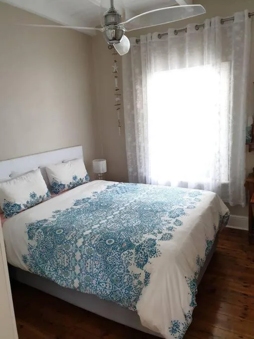 Bright bedroom with queen bed, blue patterned duvet, ceiling fan, large window