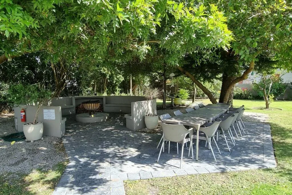 Outdoor braai and dining area under mature trees with seating for twelve