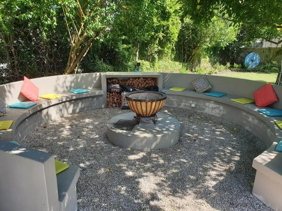 Outdoor fire pit seating area with colorful cushions and shade trees