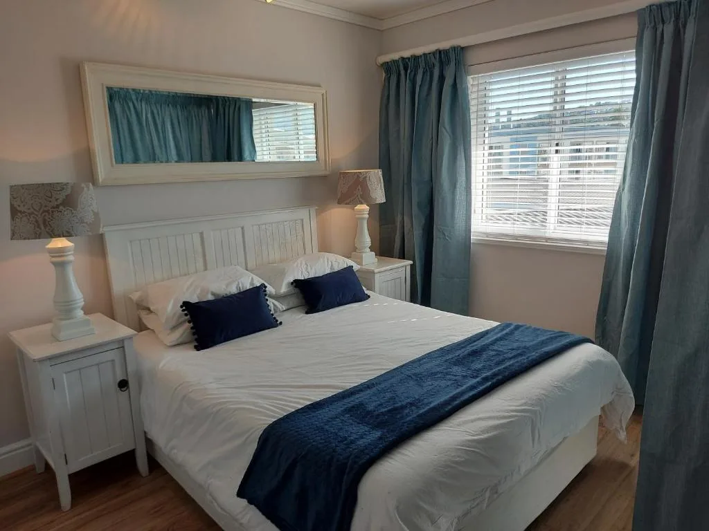 Bright bedroom with white bed frame, blue accent pillows and runner, large windows with teal curtains