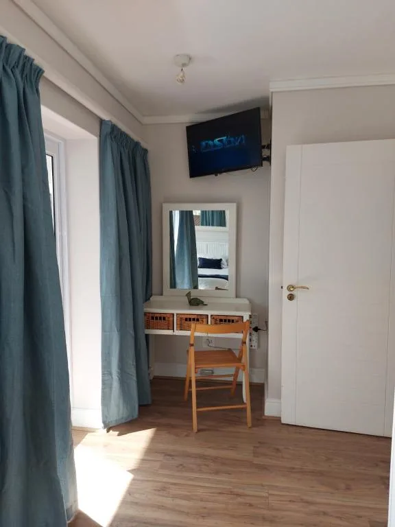 Bedroom with desk, mirror, TV, wooden chair, and teal curtains