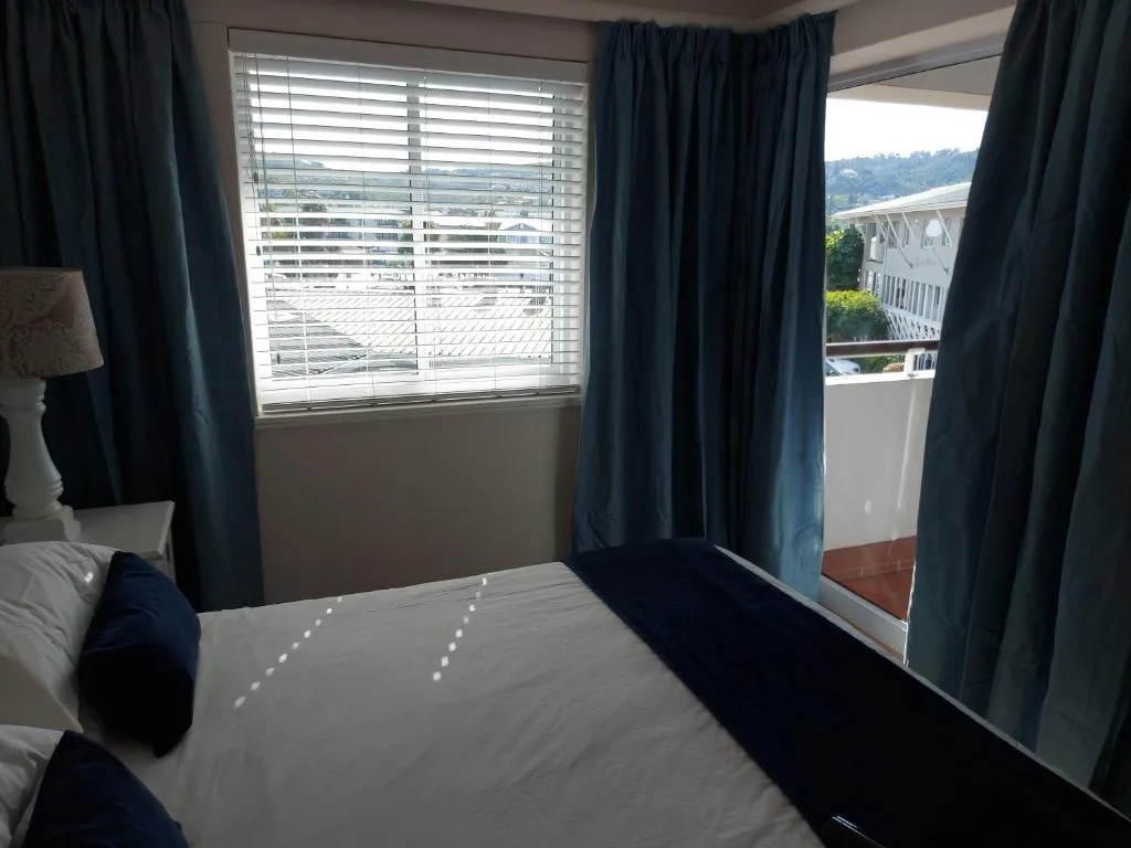 Bedroom with bed, blue curtains, and panoramic window view of lagoon
