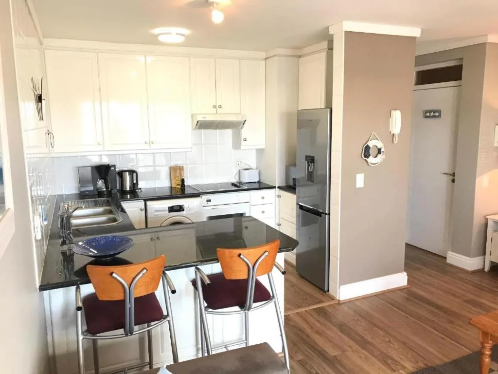 Modern kitchen with white cabinetry, black countertops, and orange bar stools