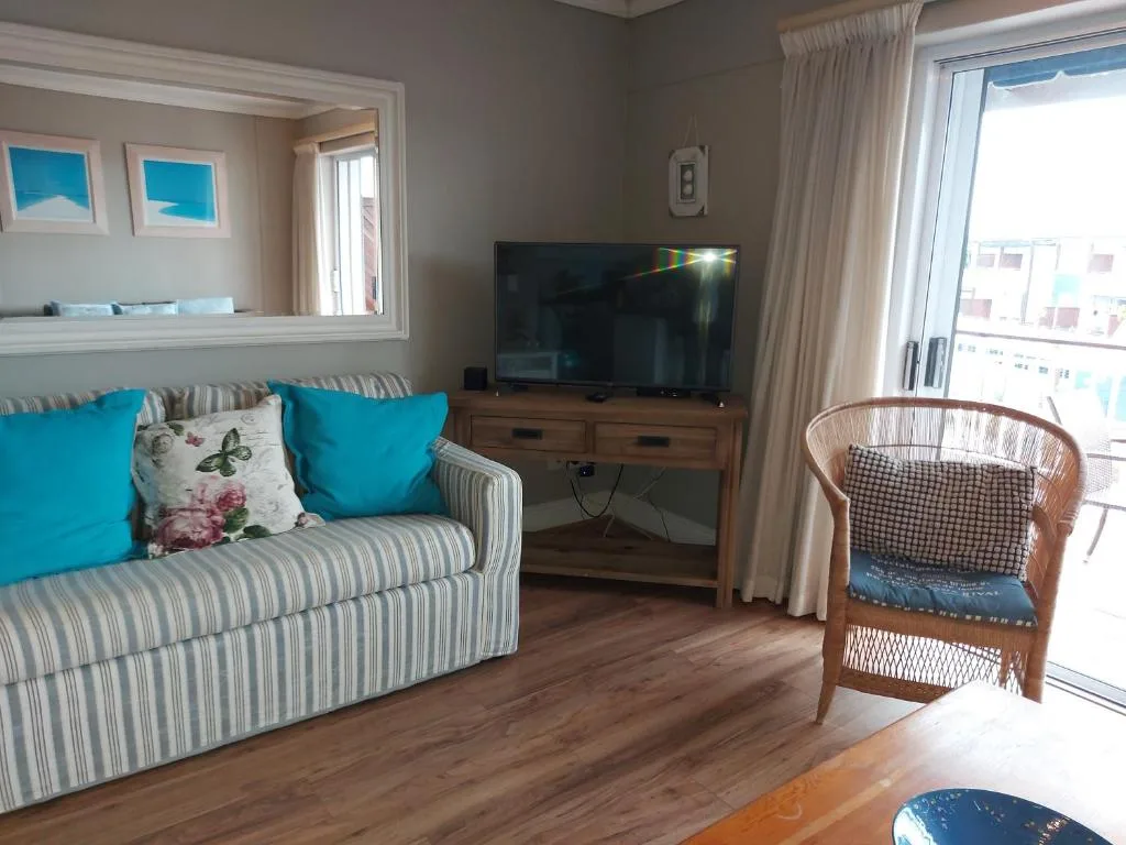 Bright lounge with striped sofa, turquoise cushions, flat-screen TV, and ocean views through glass doors